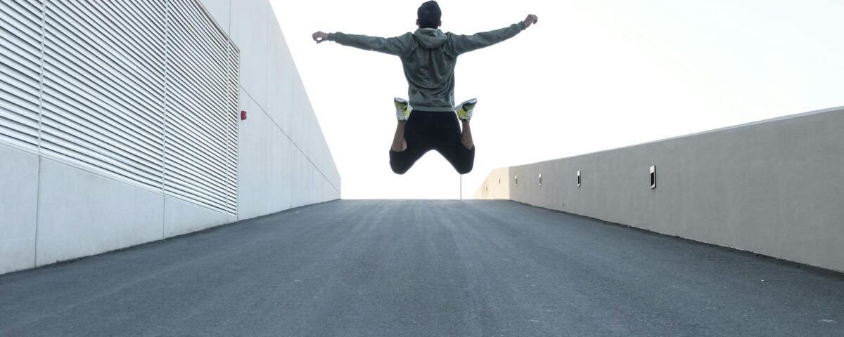 man in gray hoodie jump with open arms