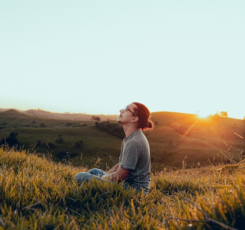 man in white shirt sitting on green grass field during sunset